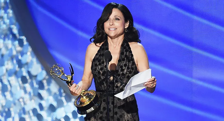 A person holding an Emmy award and a speech on stage, smiling at the audience.