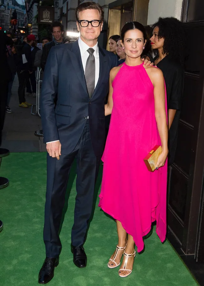Man in a suit with glasses and a woman in a pink dress on a green carpet at an event.