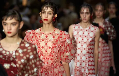 Models walking in a fashion show, wearing floral-patterned dresses in red and white.