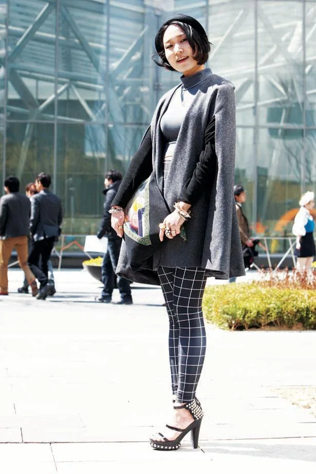 Street-style fashion in South Korea; woman in grey cape, high heels, and checkered leggings, standing outside.