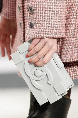 A woman holding a gray, geometric designer clutch with a pink tweed coat, showcasing chic fashion.