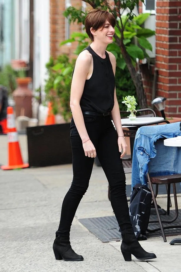 A person wearing black attire and boots walks on a sidewalk beside a table with a denim jacket draped over a chair.