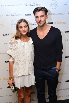 A stylish couple poses together at a Girl Most Likely event, woman in white lace, man in black shirt.