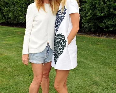 Gwyneth Paltrow and Stella McCartney posing together outdoors on grass with green foliage in the background.