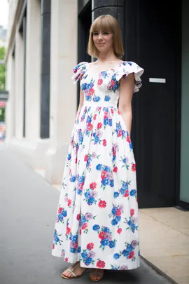 Woman in a floral maxi dress with ruffled sleeves standing on the street outside a building.