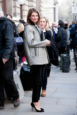 Woman in a stylish gray coat and black heels on a busy London street during fashion week.