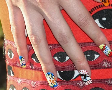 Hand with colorful, comic-style nail art rests on a dress with a pattern of large eyes.