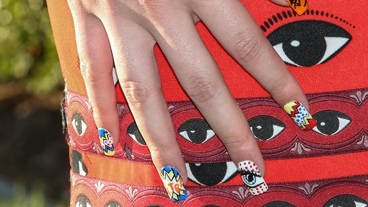 Hand with colorful, comic-style nail art rests on a dress with a pattern of large eyes.