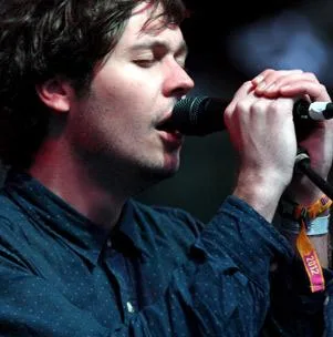 Singer performing on stage, wearing a dark blue shirt and holding a microphone.