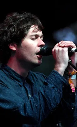 Singer performing on stage, wearing a dark blue shirt and holding a microphone.