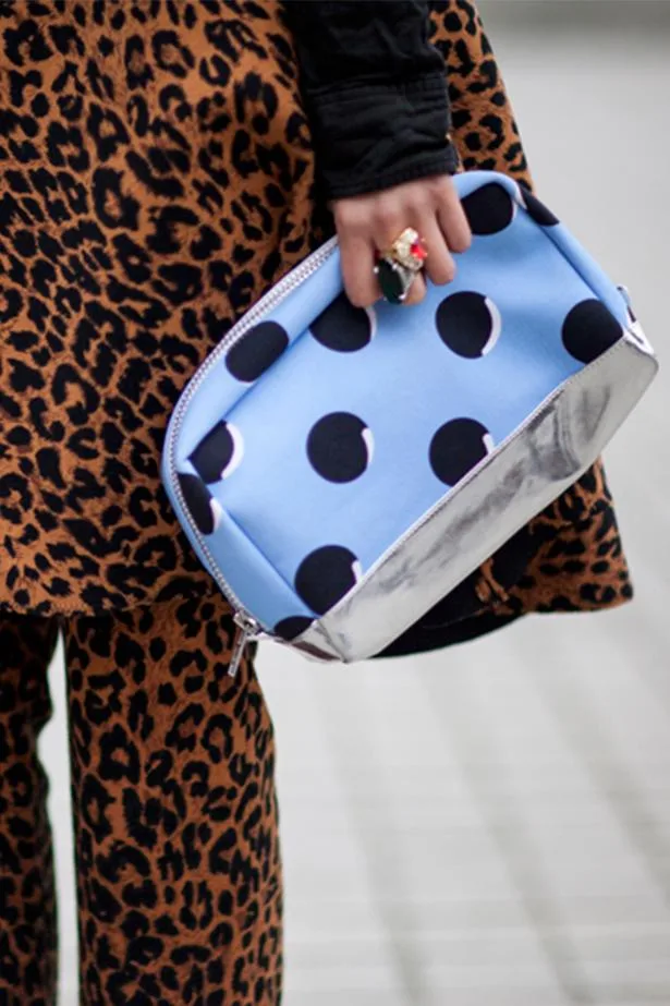 Close-up of a person holding a blue pouch with black polka dots, wearing a leopard print outfit.