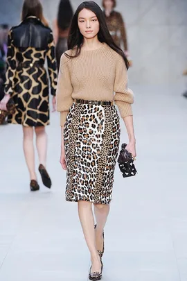 Model in a camel sweater and leopard print skirt walks the runway, holding a matching clutch.