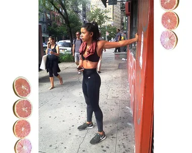 Woman in black athletic attire stretching on a city street, with a red towel around her neck and people walking in the background.