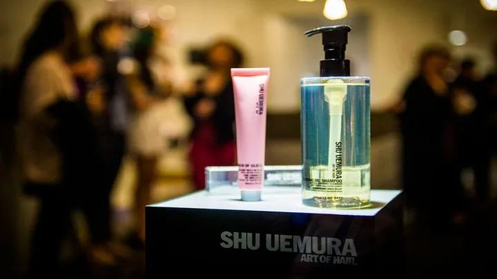 Shu Uemura hair products displayed on a stand with blurry people in the background.