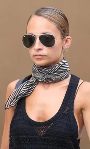 A person wearing sunglasses and a black mesh top with a black and white striped neck scarf, neutral background.