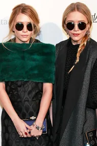 Two women in fashion-forward outfits wearing round sunglasses, posing together at an event.