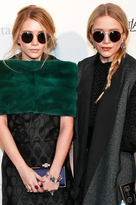 Two women in fashion-forward outfits wearing round sunglasses, posing together at an event.