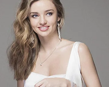 Miranda Kerr wearing Swarovski jewelry, including earrings and necklaces, smiling in a white top.