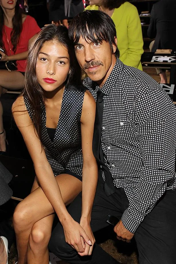 Man and woman sitting front row at New York Fashion Week, both in black and white patterned outfits.