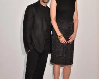 A woman in a black dress and red heels stands with a man in a black suit at a Calvin Klein event.