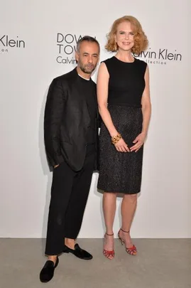 A woman in a black dress and red heels stands with a man in a black suit at a Calvin Klein event.