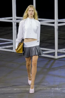 Model walks runway in white blouse, gray pleated skirt, and pink heels at Alexander Wang SS14 fashion show.