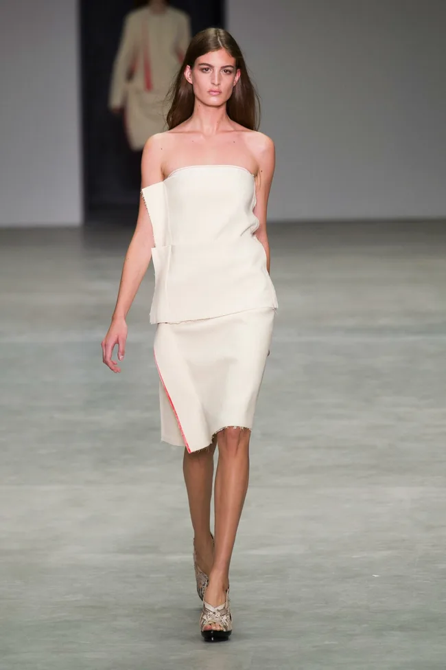 Model walking Calvin Klein Collection runway in an off-white, strapless dress during Spring/Summer 2014 fashion show.