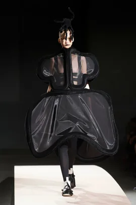 Model in avant-garde black sheer outfit with sculptural silhouette, on runway.