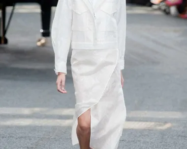 Model in a white outfit walking on a runway with a piano in the background at Erdem Spring/Summer 2014 fashion show.