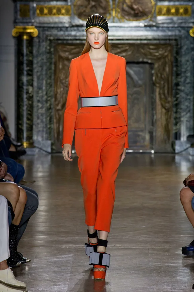 Model in an orange suit and headpiece walks the runway at John Galliano Spring/Summer 2014 fashion show.