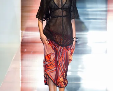 Model walks the runway wearing a black mesh top and red patterned skirt during Gucci Spring/Summer 2014 fashion show.