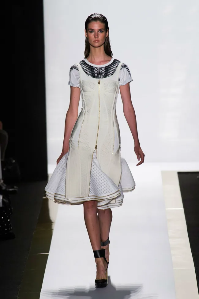 Model wearing a fitted white dress with front zip detail at Herve Leger by Max Azria SS14 show on runway.