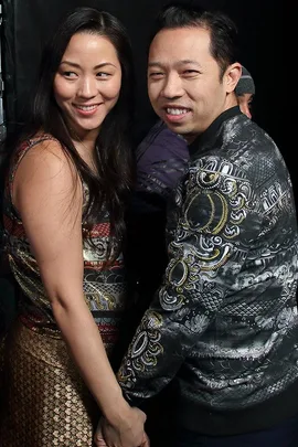 Two people holding hands and smiling at the camera at a fashion event.