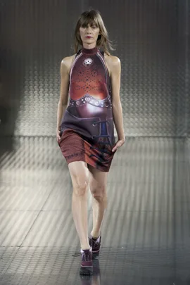 Model walking in a futuristic, patterned sleeveless dress on a metallic runway.