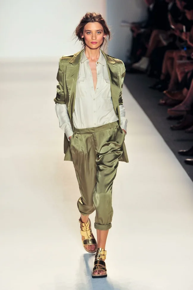 Model walks runway in olive silk suit and gold sandals at Rachel Zoe SS14 fashion show.