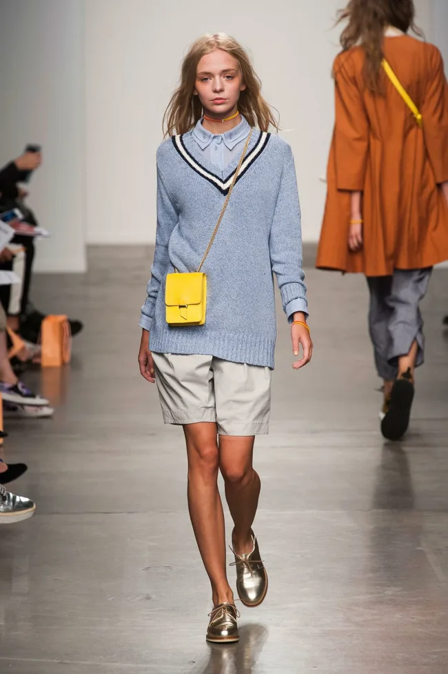 Model in blue sweater and shorts with a yellow crossbody bag, walking the runway at Karen Walker SS14 fashion show.