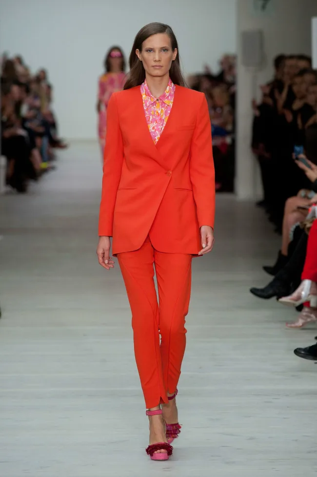 Model walks runway in red suit with floral blouse, purple heels at Matthew Williamson SS14 fashion show.