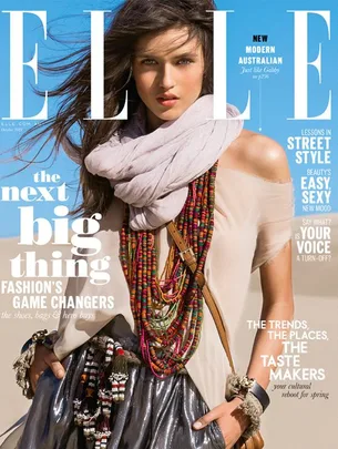 Cover of Elle magazine featuring a woman in a beige top, colorful scarf, and layered necklaces against a blue sky background.