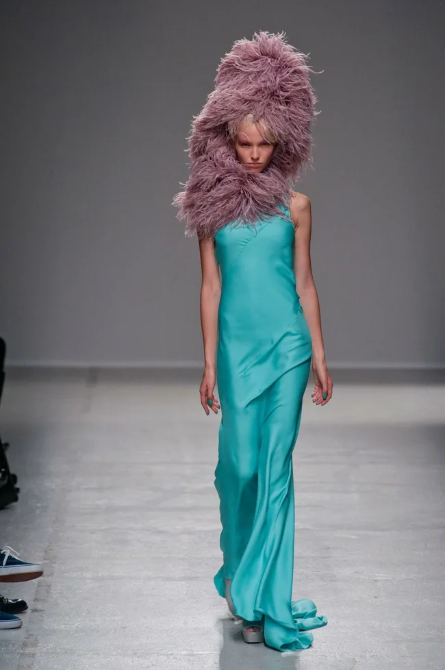 Model in teal gown with large pink fluffy headpiece walks runway, Gareth Pugh SS14 collection.