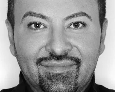 A black-and-white portrait of Napoleon Perdis, a makeup artist, smiling directly at the camera.