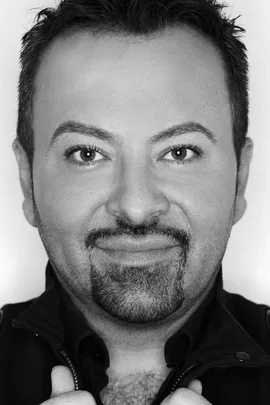 A black-and-white portrait of Napoleon Perdis, a makeup artist, smiling directly at the camera.