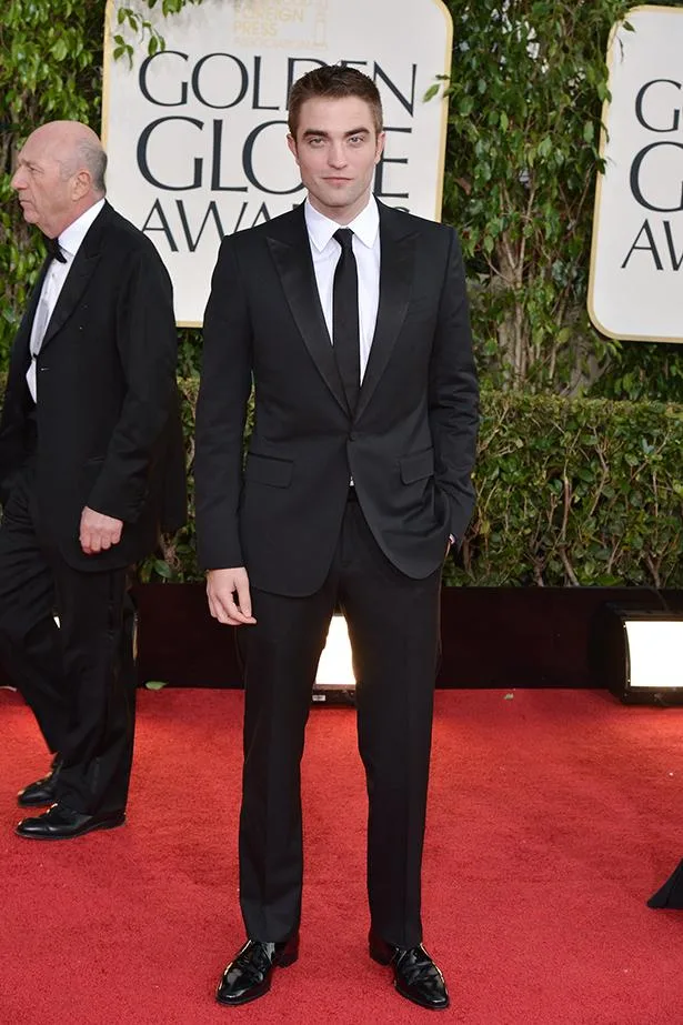 Man in a sharp black tuxedo at a red carpet event, Golden Globe Awards logo visible in the background.