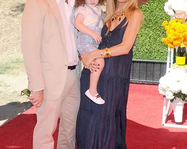 Man, woman, and child in stylish hats at a Veuve Clicquot polo event, standing on a red carpet background.