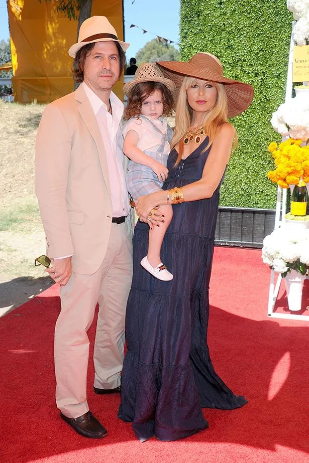 Man, woman, and child in stylish hats at a Veuve Clicquot polo event, standing on a red carpet background.