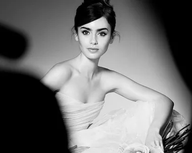 Black and white image of a woman in an elegant strapless gown holding roses, posing for a photoshoot.