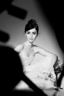 Black and white image of a woman in an elegant strapless gown holding roses, posing for a photoshoot.