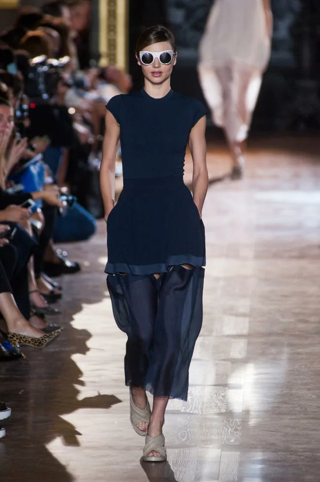 Model walking down the runway wearing a navy dress and large sunglasses at Stella McCartney SS14 fashion show.