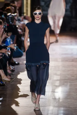 Model walking down the runway wearing a navy dress and large sunglasses at Stella McCartney SS14 fashion show.