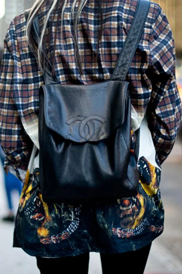 Person in plaid shirt wearing a black leather backpack with designer logo, featuring a printed graphic on the lower shirt.