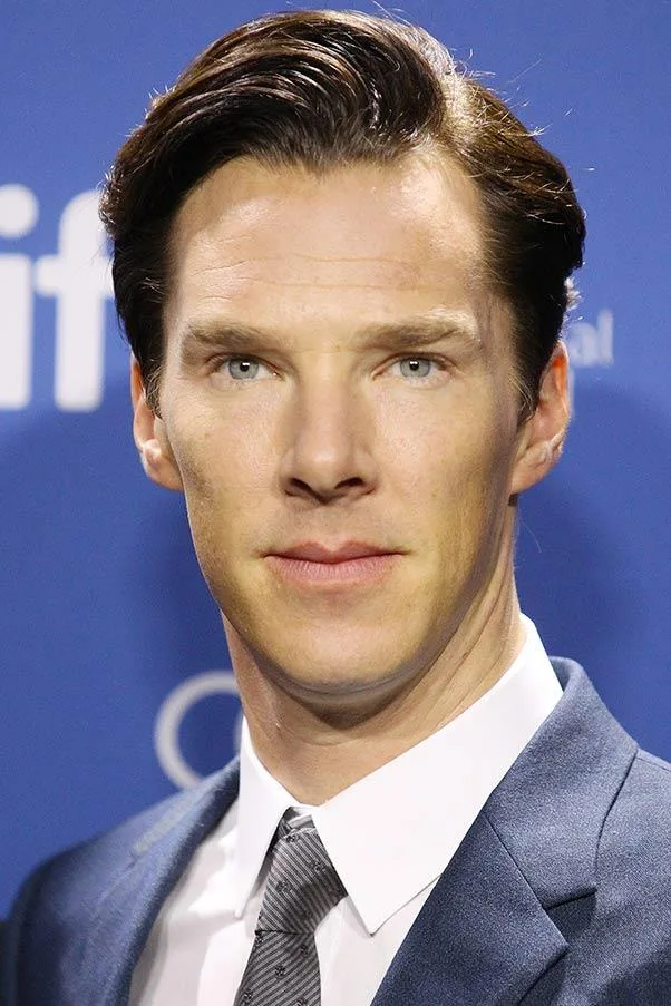 A man in a suit with short, dark hair stands against a blue background at an event.